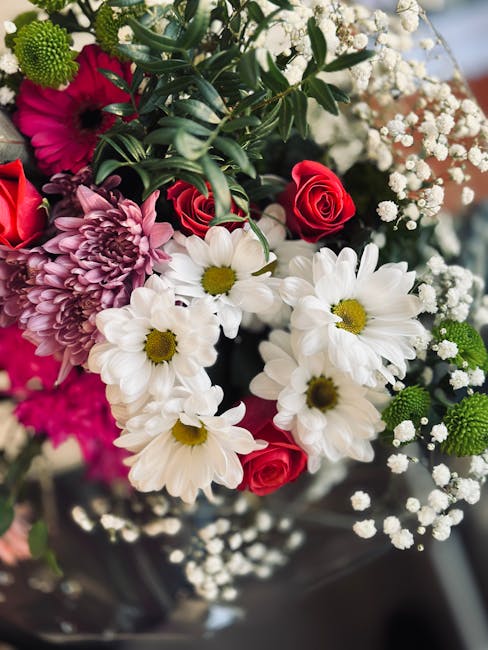 A close-up of a vibrant floral bouquet featuring white daisies with yellow centers, deep pink roses, and large mauve chrysanthemums, accented with sprigs of delicate white baby's breath and lush green