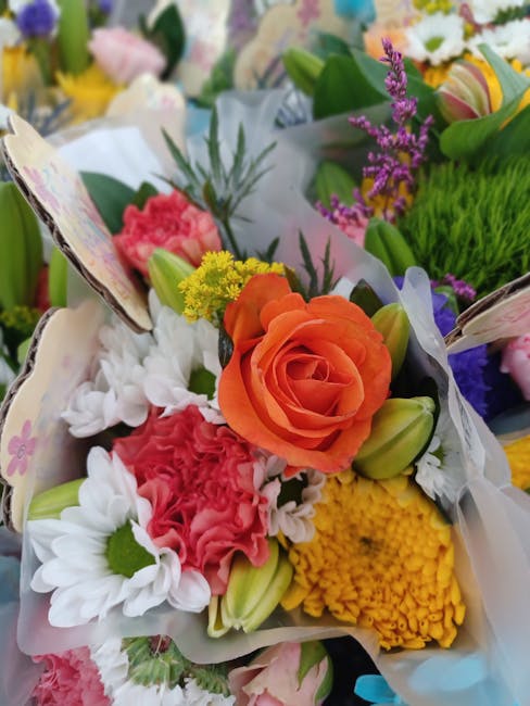 A vibrant floral bouquet featuring a prominent orange rose at the center, surrounded by white daisies with green centers, pink carnations, yellow chrysanthemum, and purple lavender sprigs, all careful